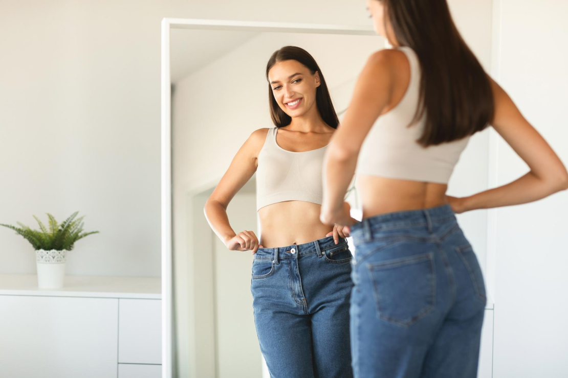 A woman happily looking at her reflection in a mirror, symbolizing successful weight loss through visualization.