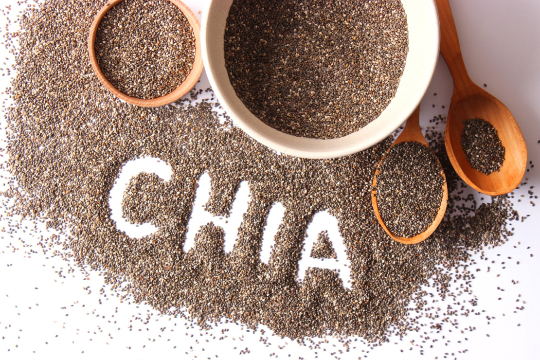 Chia seeds in a wooden spoon with a bowl of chia pudding in the background, symbolizing their versatility and nutritional power.