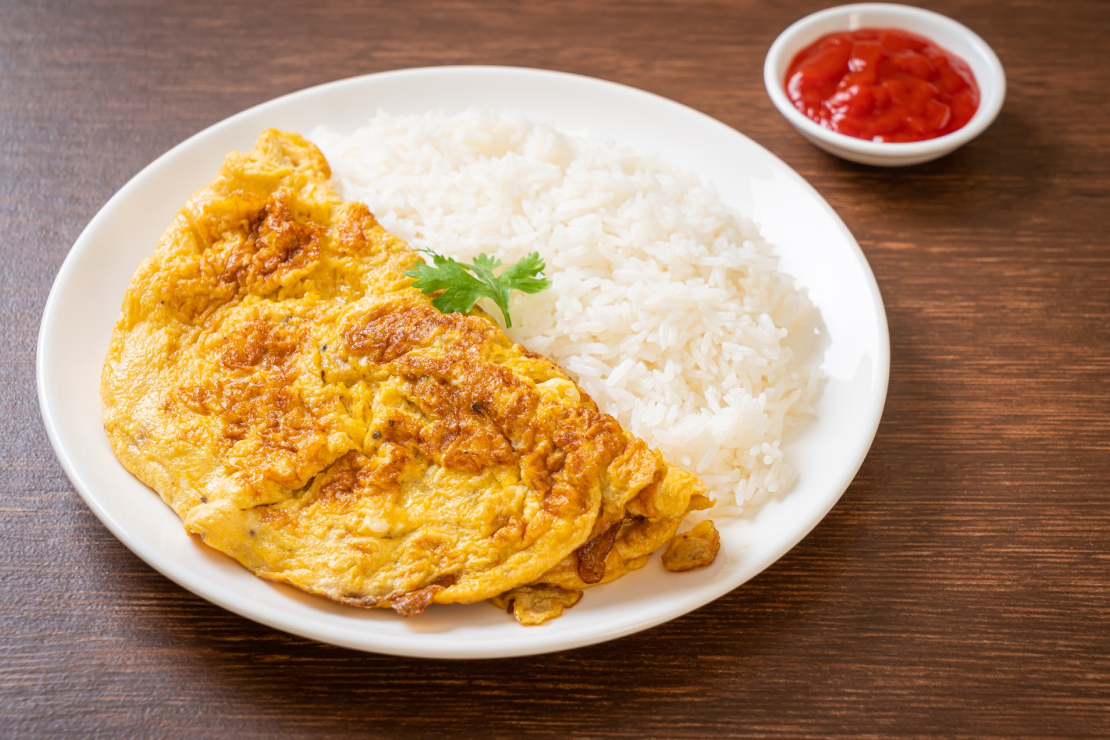 A plate of omelet and rice with a side of ketchup