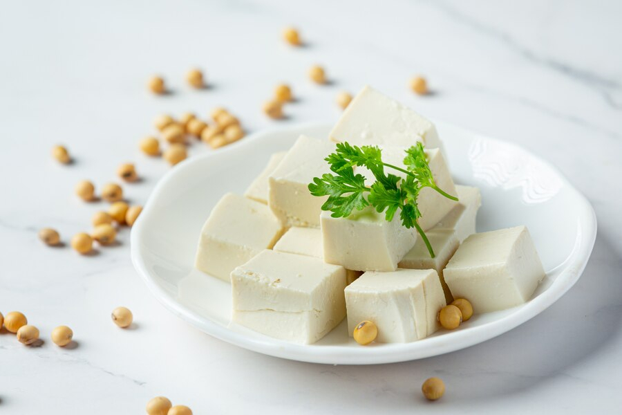 Firm tofu cubes on a white plate with fresh herbs, ready for cooking.