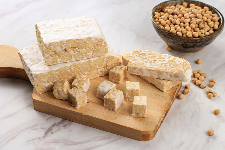 Blocks of tempeh on a wooden cutting board with soybeans, highlighting its fermented texture.